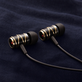 QuietBeam X in Champagne Gold — two earbuds on navy linen